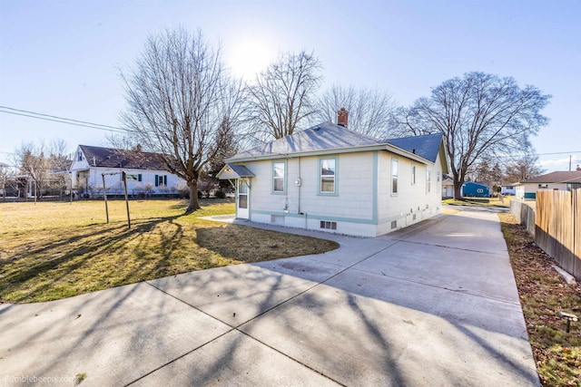 bungalow-style house with concrete driveway, a front lawn, a chimney, and fence