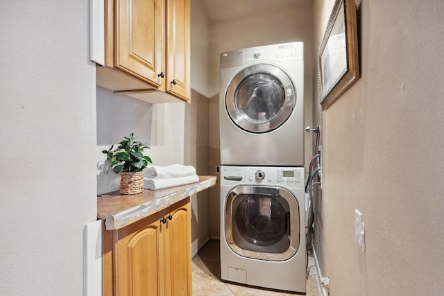 clothes washing area with light tile patterned floors, stacked washer and dryer, and cabinet space