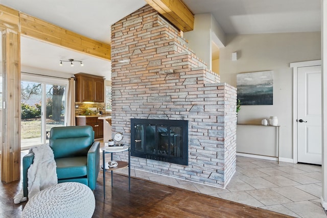 living area with a stone fireplace, beamed ceiling, and baseboards