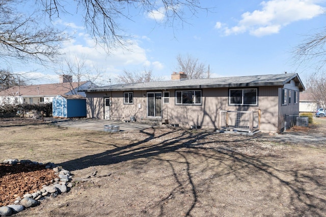 view of front of home featuring entry steps, a storage shed, a chimney, an outbuilding, and a patio area