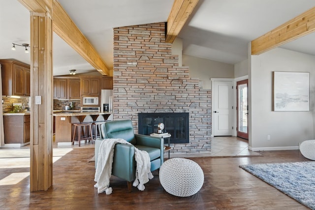 living area with lofted ceiling with beams, light wood-style floors, a fireplace, and baseboards