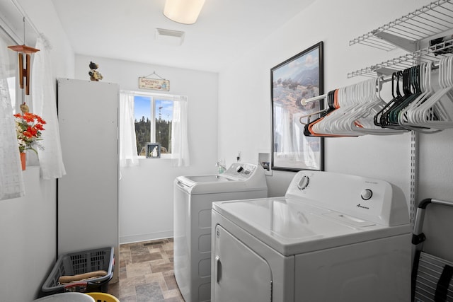 clothes washing area with laundry area, visible vents, baseboards, stone finish flooring, and washer and dryer