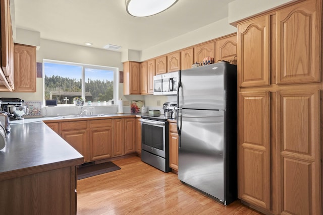 kitchen with appliances with stainless steel finishes, a sink, visible vents, and light wood-style floors