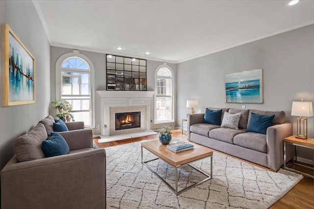 living room featuring wood finished floors, baseboards, recessed lighting, a glass covered fireplace, and crown molding