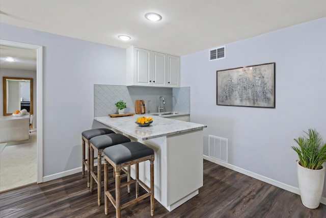 kitchen with a sink, backsplash, visible vents, and white cabinets