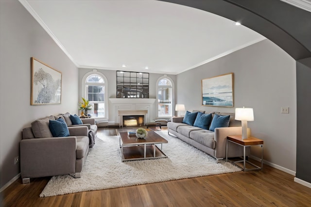 living room with wood finished floors, baseboards, a fireplace with raised hearth, arched walkways, and crown molding