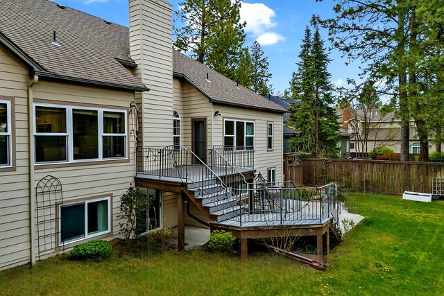 rear view of property with fence, roof with shingles, a chimney, a deck, and a yard