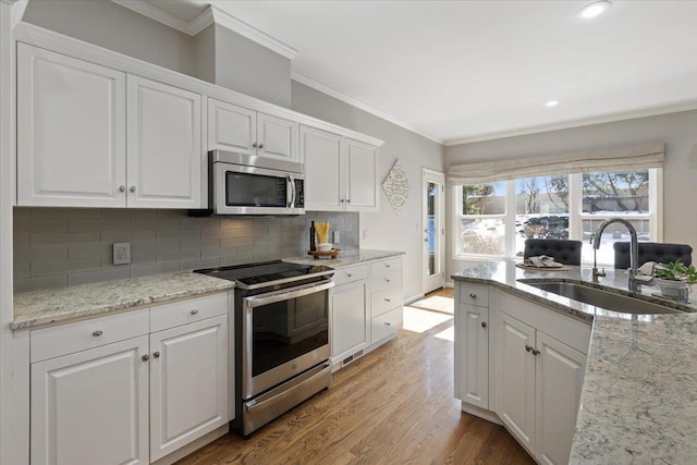 kitchen featuring ornamental molding, white cabinets, stainless steel appliances, and a sink