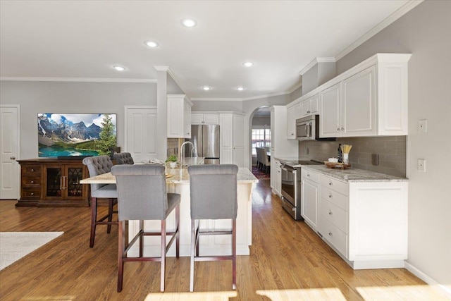 kitchen featuring stainless steel appliances, arched walkways, a breakfast bar, and light wood finished floors