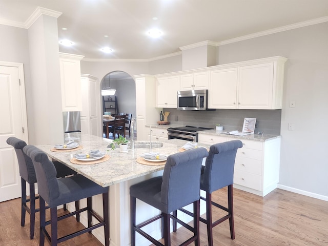 kitchen featuring light wood-type flooring, stainless steel appliances, arched walkways, and white cabinetry