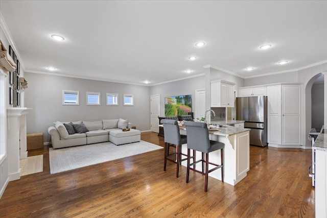 kitchen with light stone countertops, a kitchen bar, appliances with stainless steel finishes, arched walkways, and white cabinetry