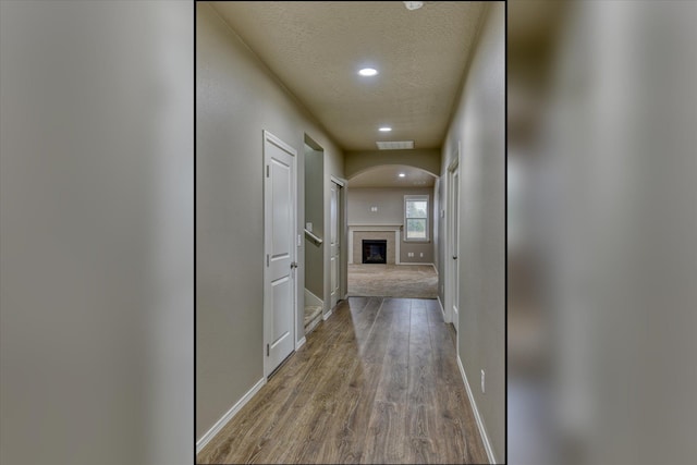 hallway with recessed lighting, visible vents, a textured ceiling, wood finished floors, and baseboards