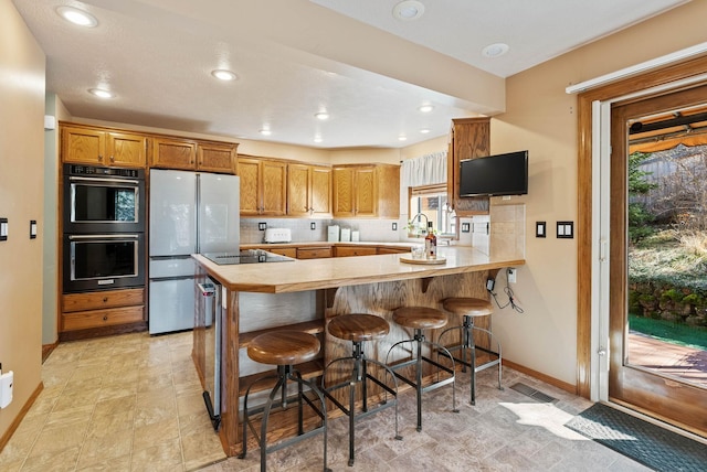 kitchen featuring a peninsula, black appliances, light countertops, and decorative backsplash