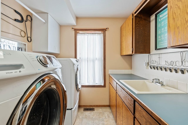 laundry room with washing machine and clothes dryer, cabinet space, visible vents, a sink, and baseboards