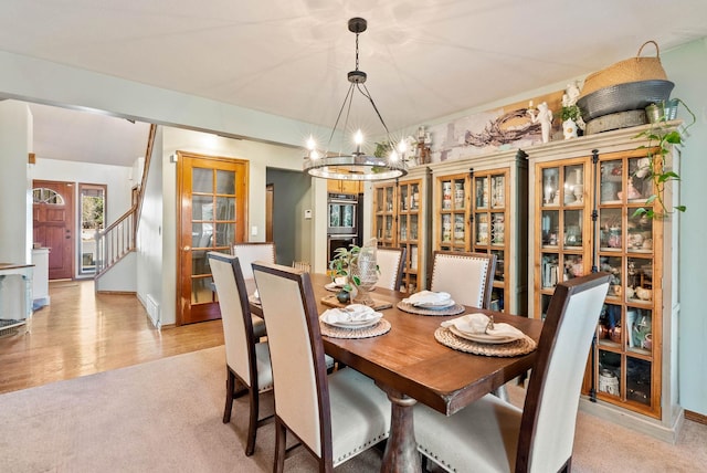 dining room with light carpet, light wood-style floors, stairway, and a notable chandelier