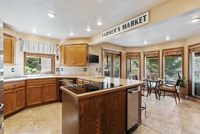 kitchen with a peninsula, a sink, black electric cooktop, and decorative backsplash