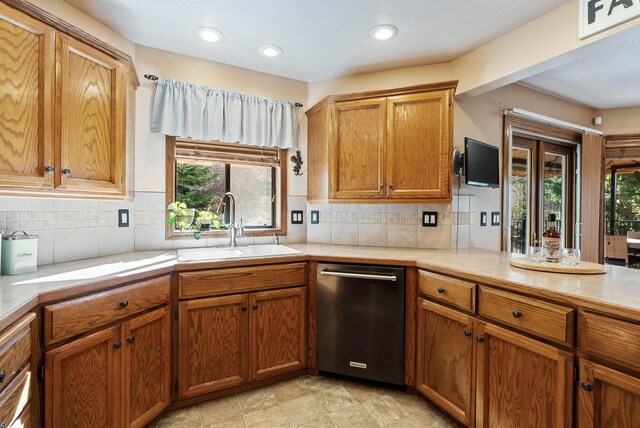 kitchen with tasteful backsplash, brown cabinetry, light countertops, stainless steel dishwasher, and a sink