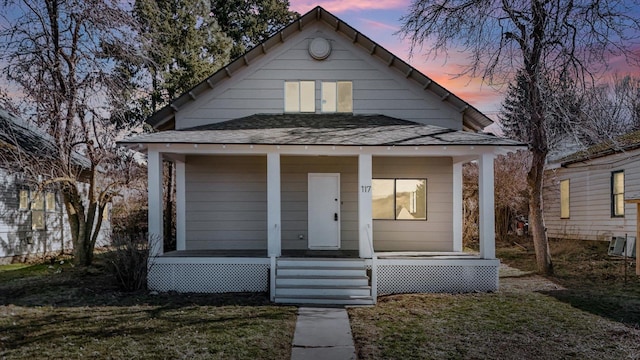 bungalow-style house with a shingled roof, a porch, and a lawn