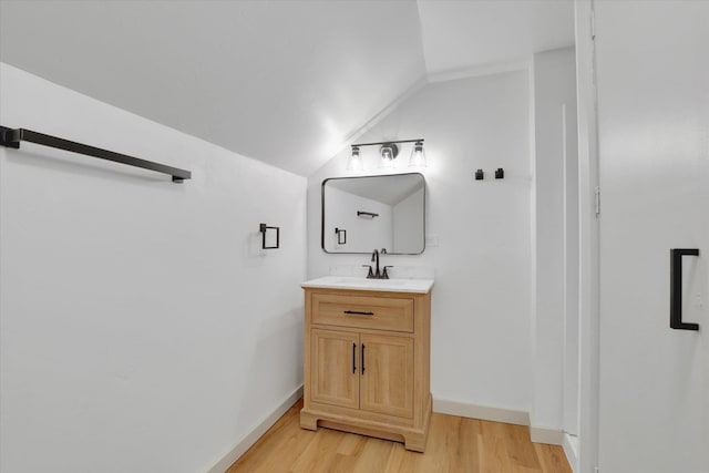 bathroom with vaulted ceiling, vanity, baseboards, and wood finished floors