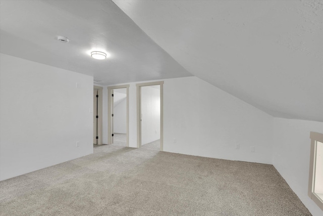 additional living space with light colored carpet and vaulted ceiling