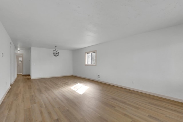 unfurnished room featuring light wood-type flooring, baseboards, and an inviting chandelier