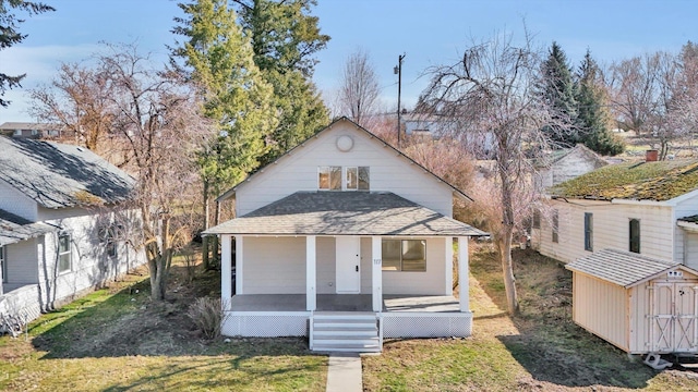 view of front of house with an outbuilding, a storage unit, a shingled roof, covered porch, and a front lawn