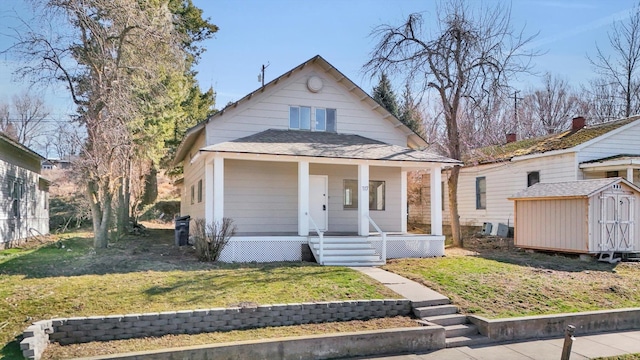 bungalow featuring a storage unit, a porch, a shingled roof, a front yard, and an outdoor structure