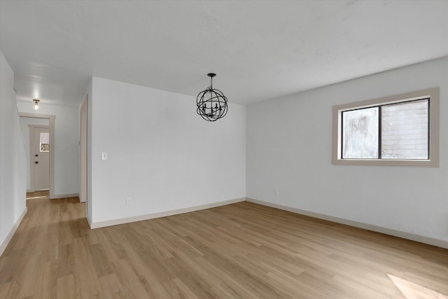 unfurnished room with a notable chandelier, baseboards, and light wood-style floors