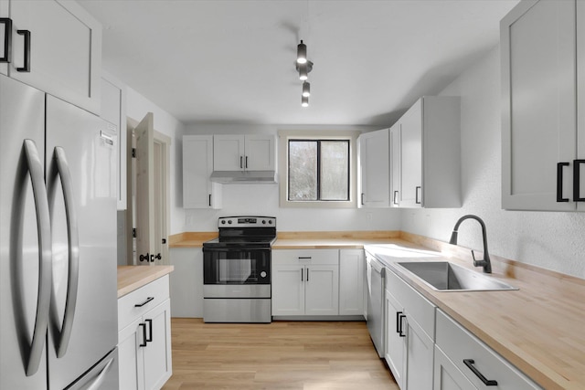 kitchen featuring under cabinet range hood, butcher block countertops, a sink, appliances with stainless steel finishes, and light wood-type flooring