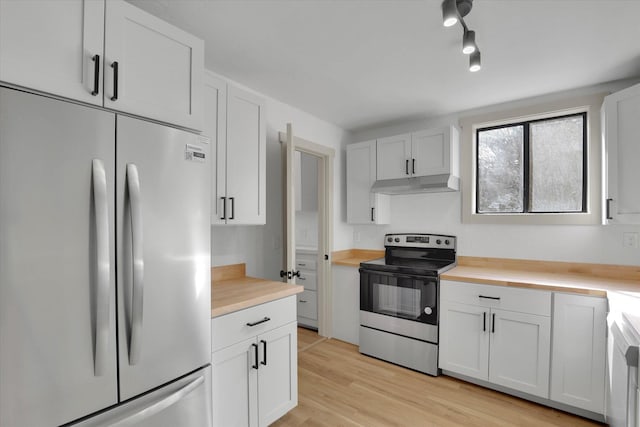 kitchen with under cabinet range hood, butcher block counters, white cabinets, appliances with stainless steel finishes, and light wood finished floors