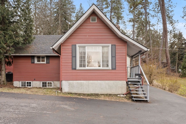 view of side of home featuring a shingled roof and aphalt driveway