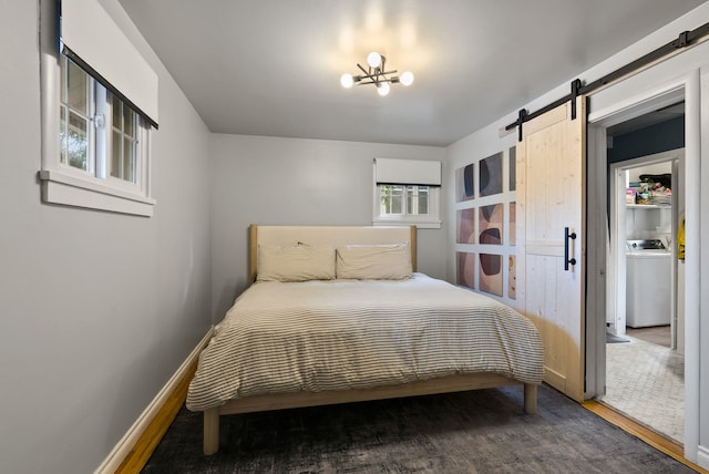 bedroom featuring a notable chandelier, washer / clothes dryer, a barn door, wood finished floors, and baseboards