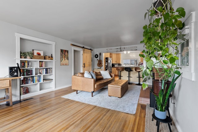 living area with baseboards, a barn door, visible vents, and light wood-style floors