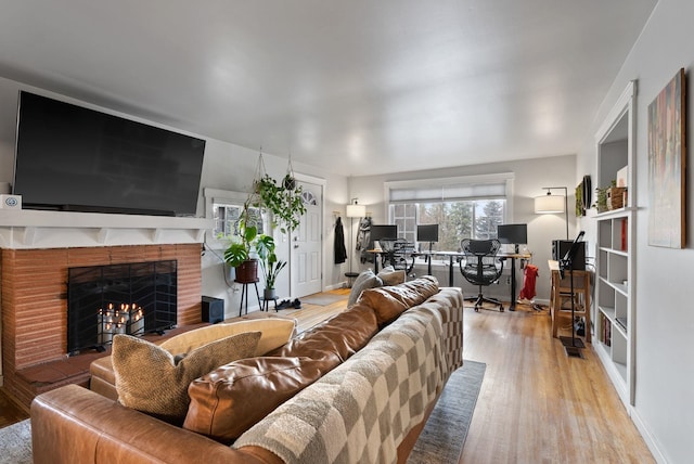 living room featuring a warm lit fireplace, baseboards, and wood finished floors