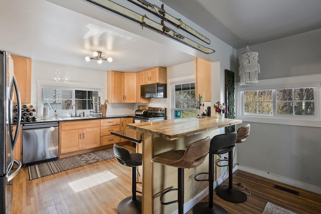 kitchen featuring visible vents, light brown cabinetry, appliances with stainless steel finishes, a sink, and wood finished floors