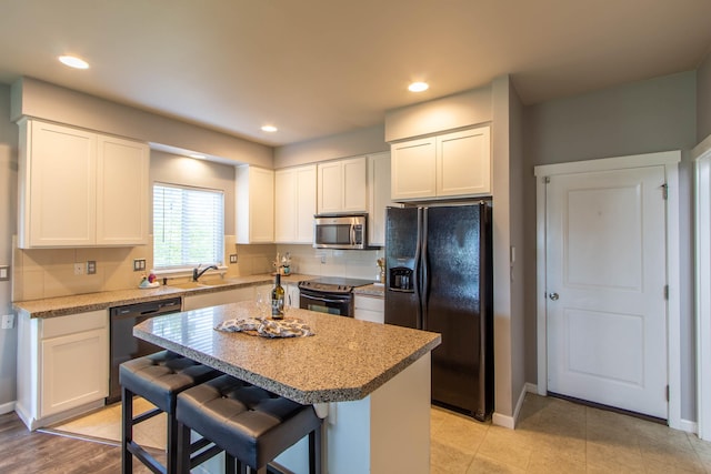 kitchen with black appliances, white cabinetry, light countertops, and a center island