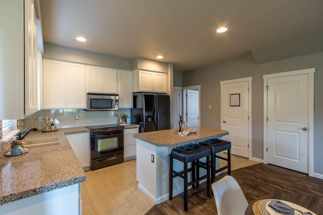 kitchen with a center island, decorative backsplash, white cabinets, a sink, and black appliances