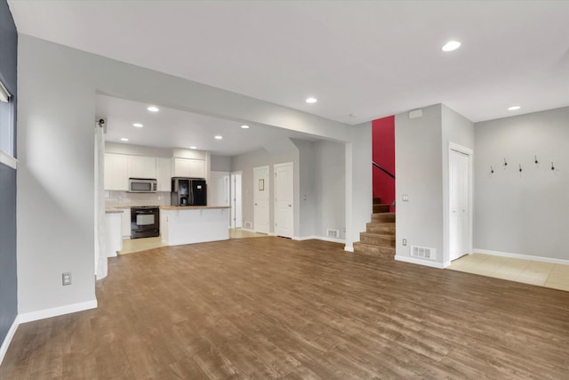 unfurnished living room with recessed lighting, visible vents, wood finished floors, baseboards, and stairs