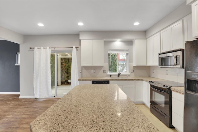 kitchen with tasteful backsplash, white cabinetry, a sink, light stone countertops, and black appliances