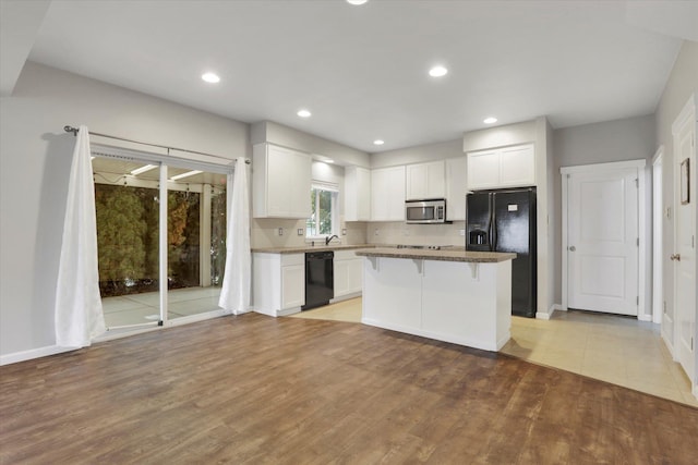 kitchen featuring a center island, a breakfast bar area, light wood-style flooring, white cabinetry, and black appliances