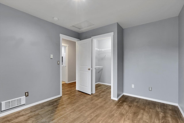 unfurnished bedroom featuring attic access, baseboards, visible vents, wood finished floors, and a closet