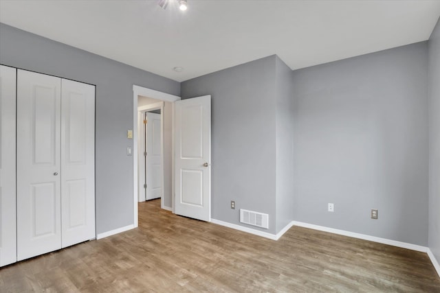 unfurnished bedroom with a closet, visible vents, baseboards, and wood finished floors