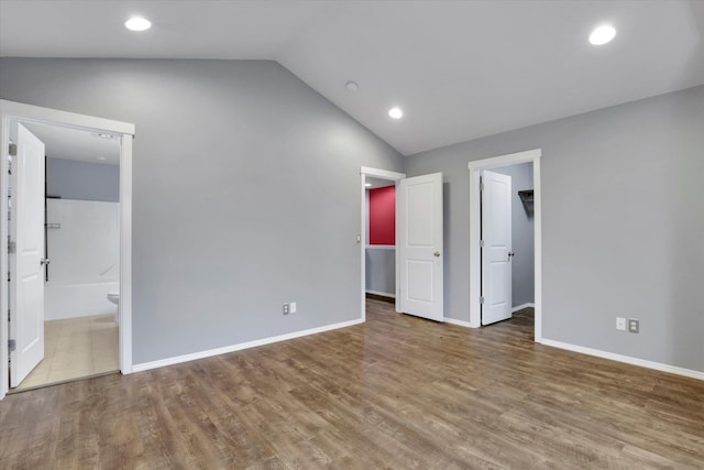 unfurnished bedroom with recessed lighting, wood finished floors, baseboards, vaulted ceiling, and a spacious closet