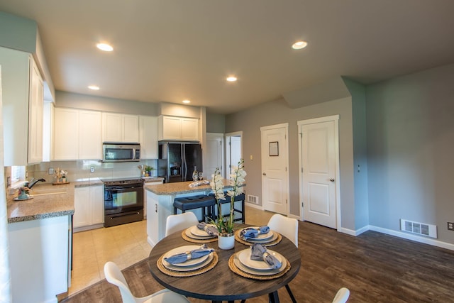 kitchen with visible vents, backsplash, white cabinetry, a sink, and black appliances