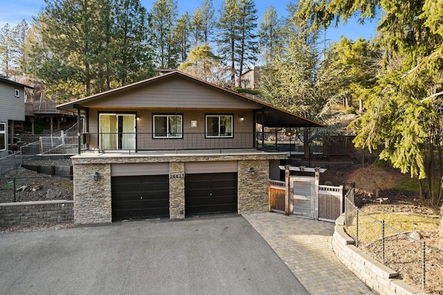 view of front of home featuring a gate, aphalt driveway, stone siding, fence, and a garage