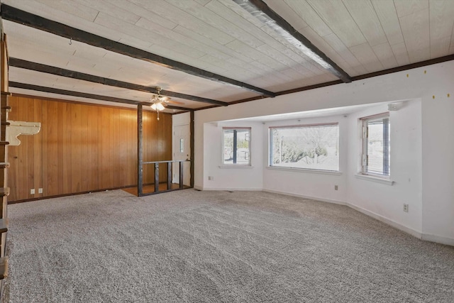 empty room featuring baseboards, ceiling fan, beamed ceiling, carpet flooring, and wood walls