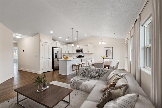 living room with lofted ceiling, a textured ceiling, a notable chandelier, dark wood-style flooring, and baseboards