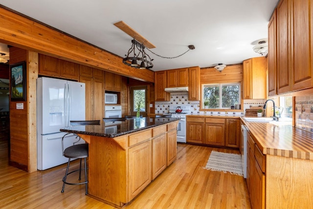 kitchen with white appliances, a kitchen island, under cabinet range hood, and light wood finished floors