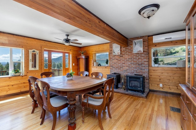 dining room with a wall mounted air conditioner, a wood stove, light wood-type flooring, wood walls, and beam ceiling