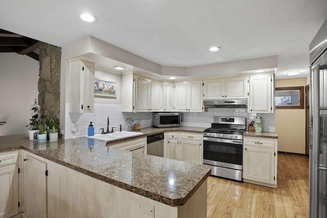 kitchen featuring under cabinet range hood, a peninsula, a sink, appliances with stainless steel finishes, and light wood finished floors